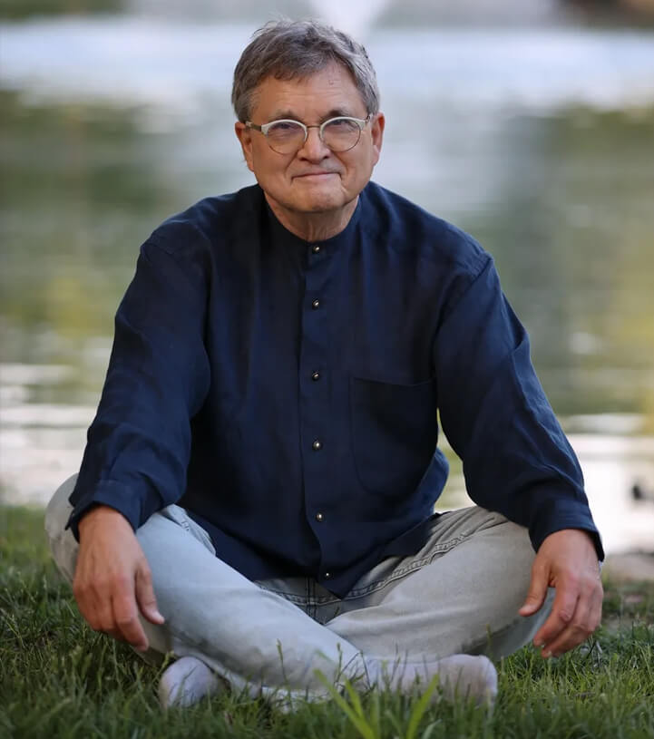 A man sitting on the grass in front of water.